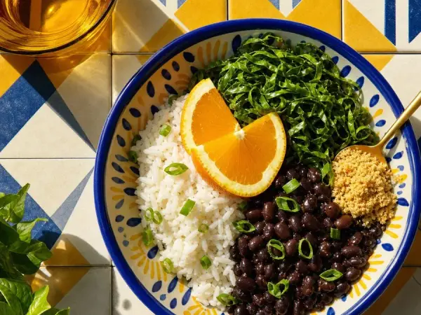 Brazilian black bean bowl with garlic rice, collard greens, orange wedges, and cassava farofa